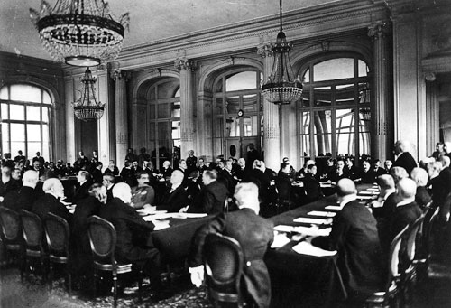 Bei den Friedensverhandlungen in Versailles, Hotel „Trianon Palace“, 7. Mai 1919: Der französische Premierminister Georges Clemenceau (rechts im Bild, stehend) trägt der deutschen Delegation die Bedingungen der Alliierten vor.