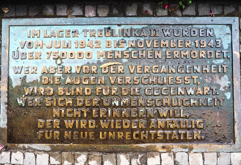 Eine 1986 ergänzte Bodenplatte mit historischer Kurzinformation und einem (nicht gekennzeichneten) Zitat aus Richard von Weizsäckers Gedenkrede zum 8. Mai 1985